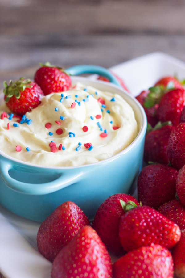 Easy Creamy Vanilla Pudding Fruit Dip in a bowl topped with sprinkles and fresh strawberries, surrounded by more fresh strawberries on a platter.  