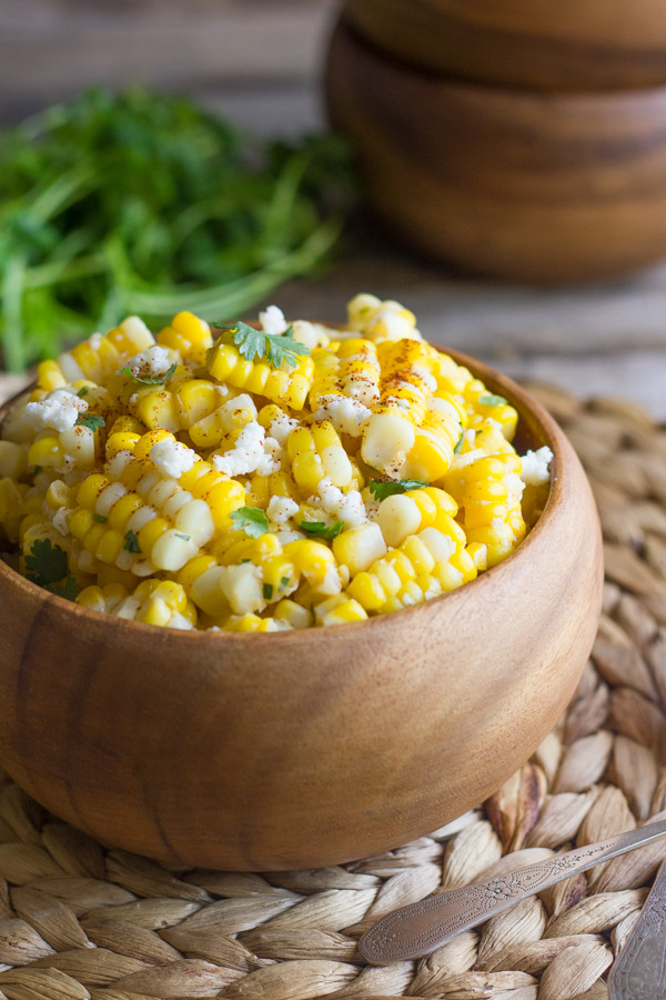 Chili Lime Sweet Corn Salad in a bowl, with a stack of bowls and a bundle of cilantro in the background.  