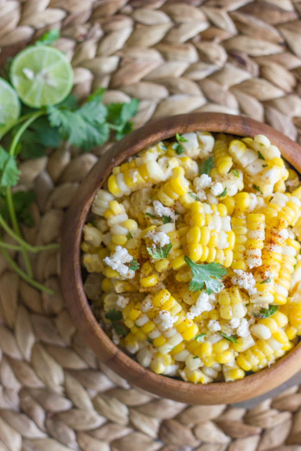 Chili Lime Sweet Corn Salad in a bowl, with a bundle of cilantro and a lime cut in half next to the bowl.  