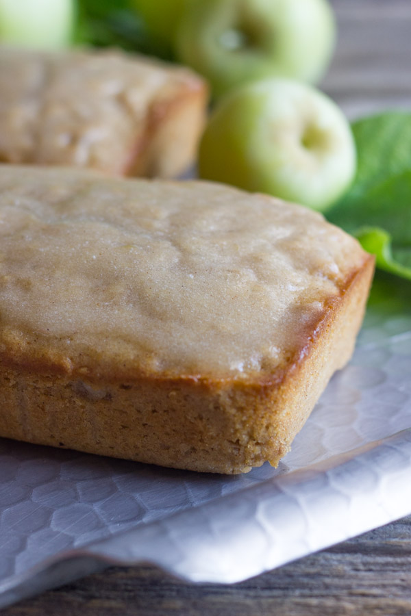 Glazed Apple Cinnamon Oatmeal Bread loaves on a serving platter, with whole apples in the background.  