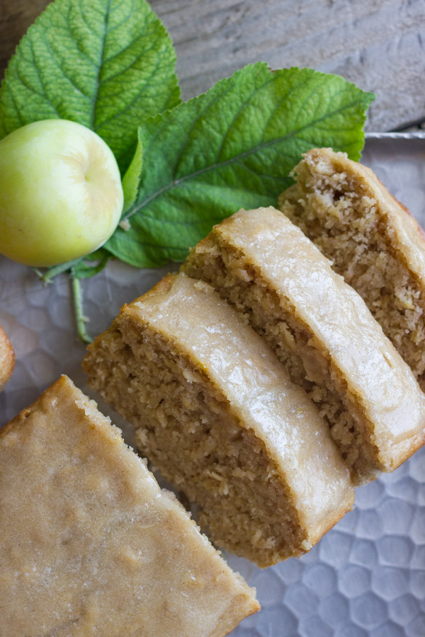 Glazed Apple Cinnamon Oatmeal Bread sliced on a serving platter, with a whole apple and leaves next to it.  