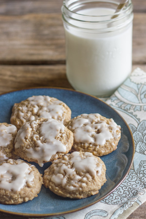 Maple Iced Oatmeal Cookies on a blue plate with a cloth napkin under it and a glass of milk next to it.  
