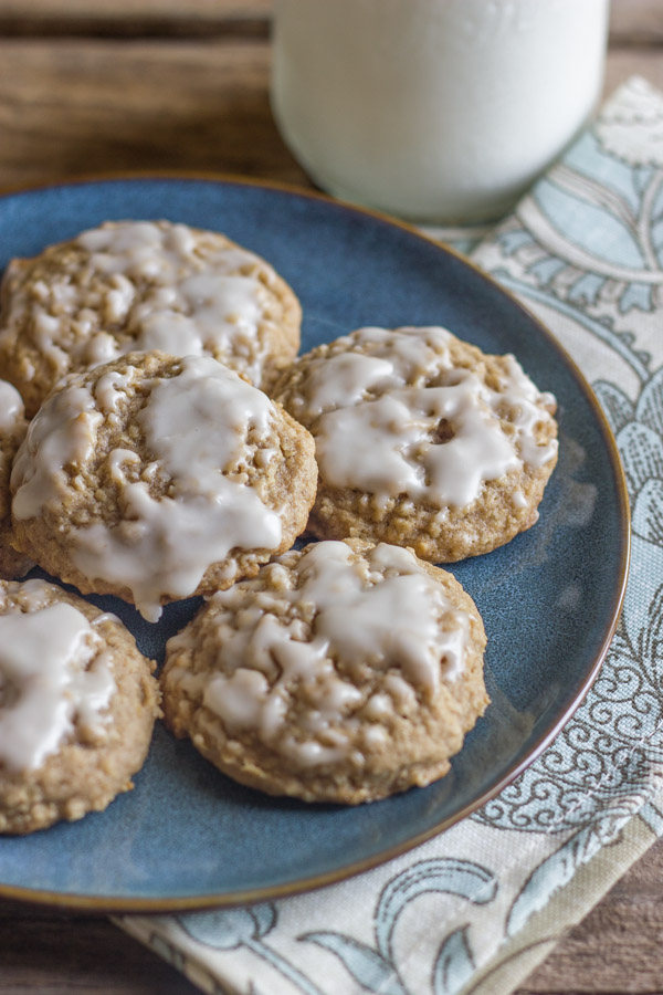 Maple Iced Oatmeal Cookies on a blue plate with a cloth napkin under it and a glass of milk next to it.  