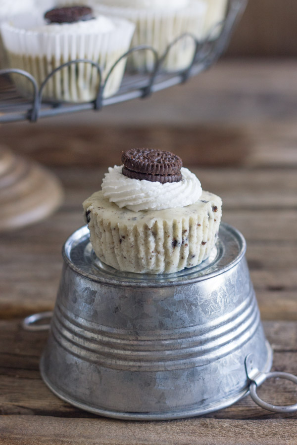 Cookies and Cream Cheesecake Cup sitting on a mini galvanized bucket that is upside down, with more Cookies and Cream Cheesecake Cups arranged on a cake stand in the background.  