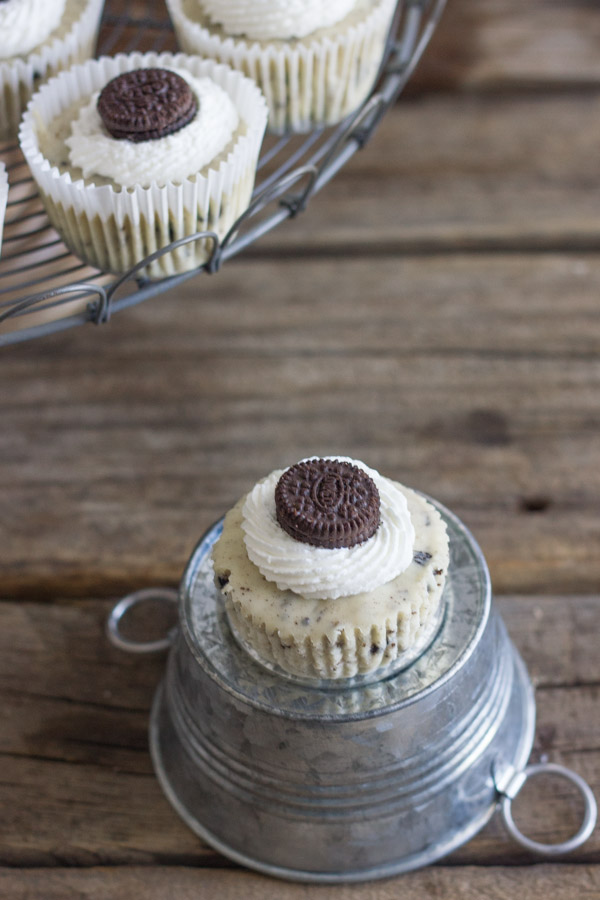 Cookies and Cream Cheesecake Cup sitting on a mini galvanized bucket that is upside down, with more Cookies and Cream Cheesecake Cups arranged on a cake stand next to it.  