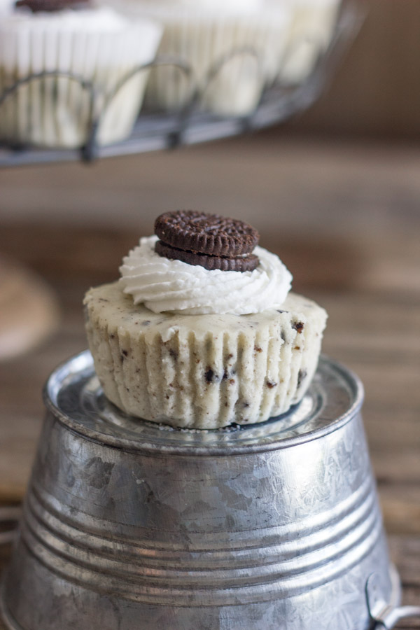Cookies and Cream Cheesecake Cup sitting on a mini galvanized bucket that is upside down, with more Cookies and Cream Cheesecake Cups arranged on a cake stand in the background.  