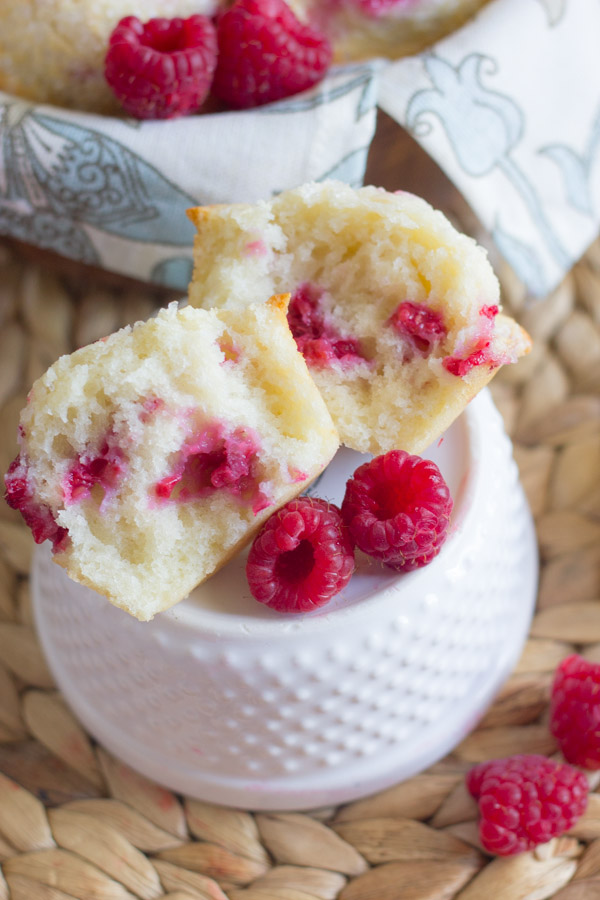 Healthier Raspberry Almond Muffin cut in half, sitting on top of a glass dish with fresh raspberries around it.