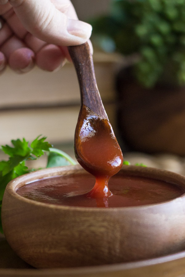 Homemade Honey BBQ Sauce in a small wood bowl, with a small wooden spoon dipped in it, with some green garnish next to it.  