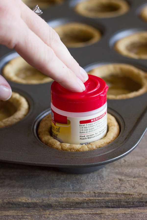 A small spice container being used to press down the center of the baked cookie dough to make the little well in the center for the Ice Cream Sundae Cookie Cups.  