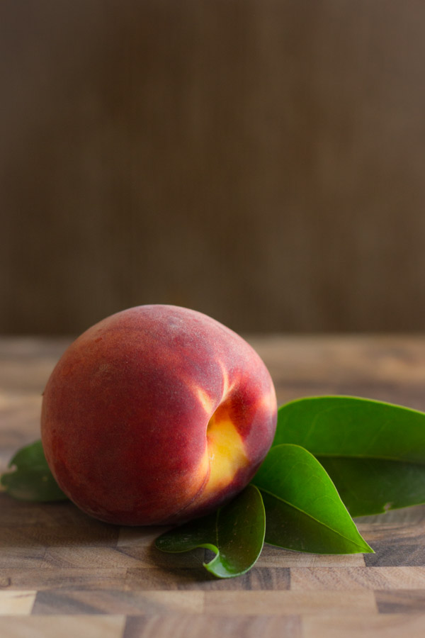 A whole peach on a cutting board.  