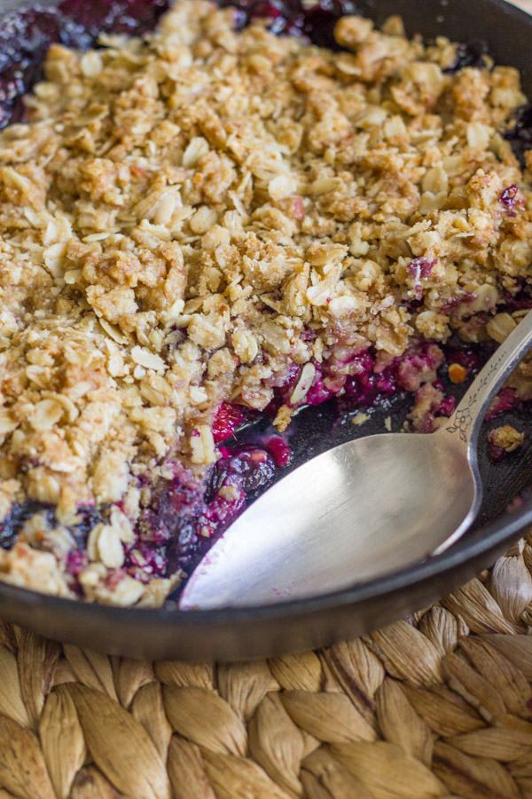 Triple Berry Skillet Crisp in a cast iron skillet with a serving spoon.  