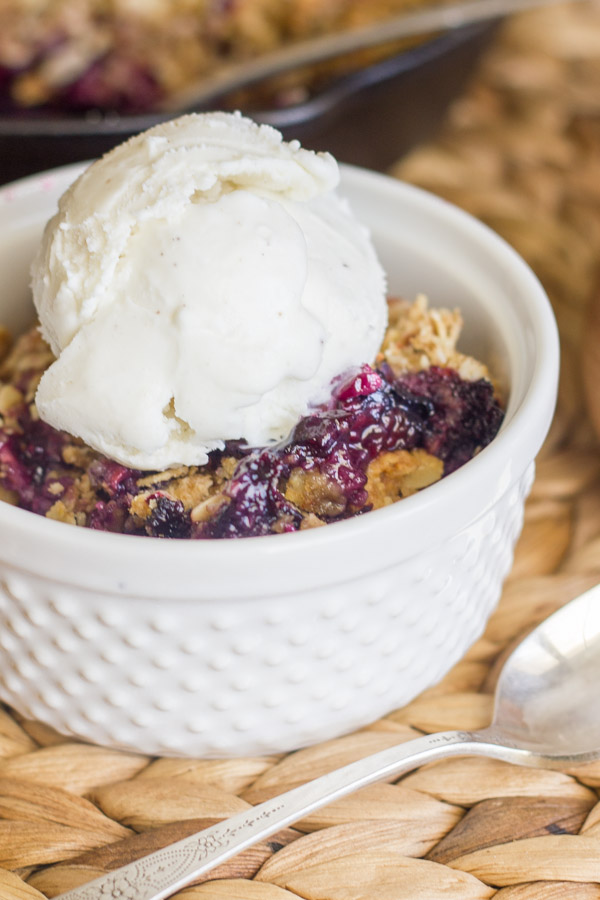 Triple Berry Skillet Crisp in a glass dish with a scoop of vanilla ice cream on top.  