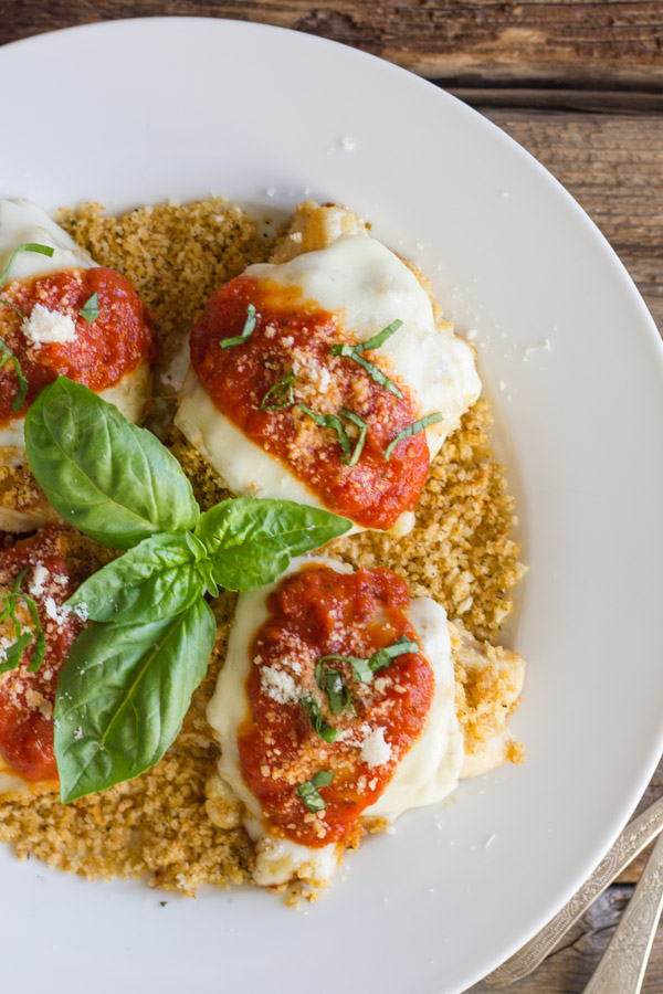 Easy Chicken Parmesan With Toasted Panko on top of a thin layer of the toasted Panko on a serving plate, topped with red sauce, grated Parmesan and some thinly sliced fresh basil, with fresh basil leaves in the center of the serving plate.  