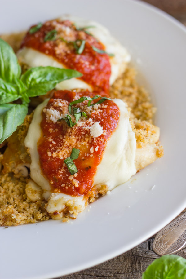 Easy Chicken Parmesan With Toasted Panko on top of a thin layer of the toasted Panko on a serving plate, topped with red sauce, grated Parmesan and some thinly sliced fresh basil, with fresh basil leaves in the center of the serving plate.  