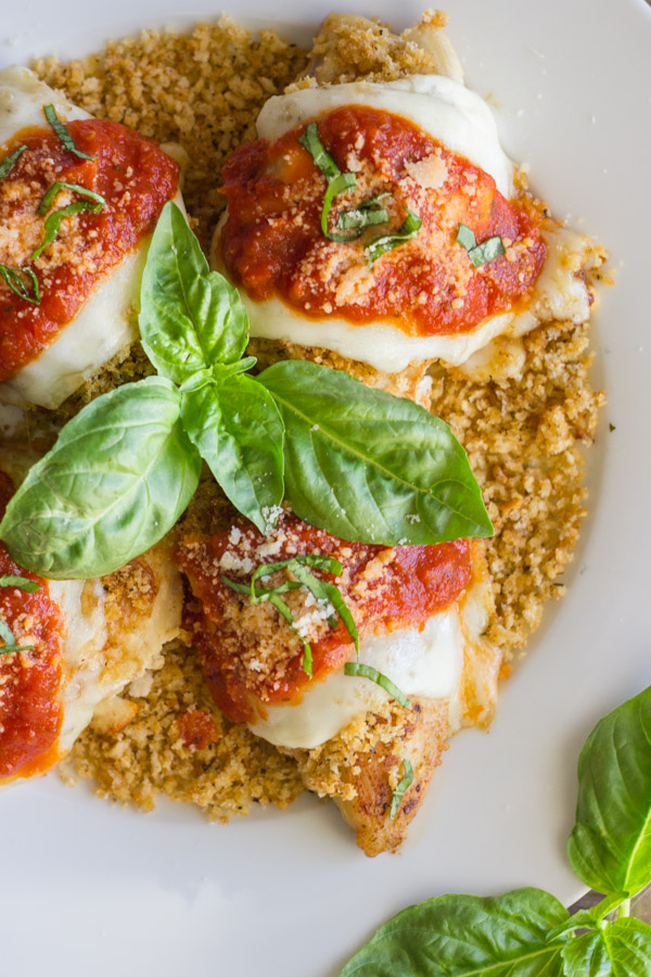 Easy Chicken Parmesan With Toasted Panko on top of a thin layer of the toasted Panko on a serving plate, topped with red sauce, grated Parmesan and some thinly sliced fresh basil, with fresh basil leaves in the center of the serving plate.  