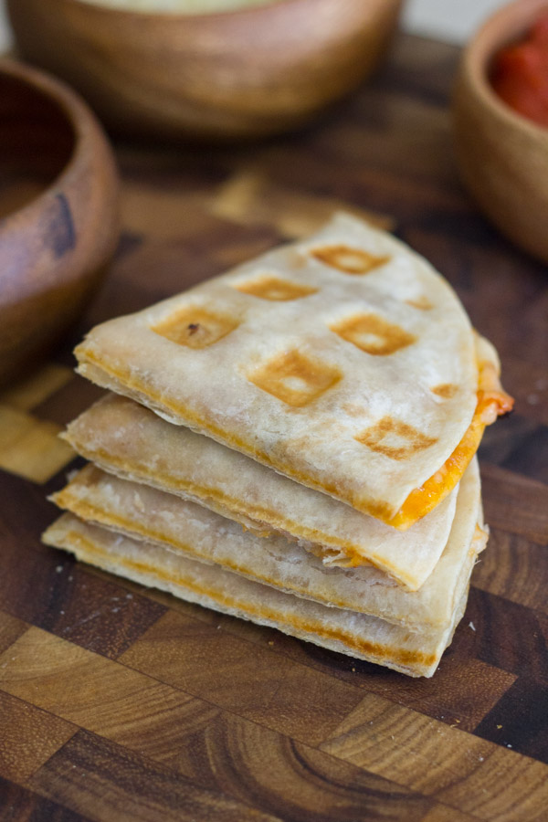 Waffled Pizza Pocket cut in four pieces and stacked in a pile on a cutting board, with bowls of ingredients in the background.  