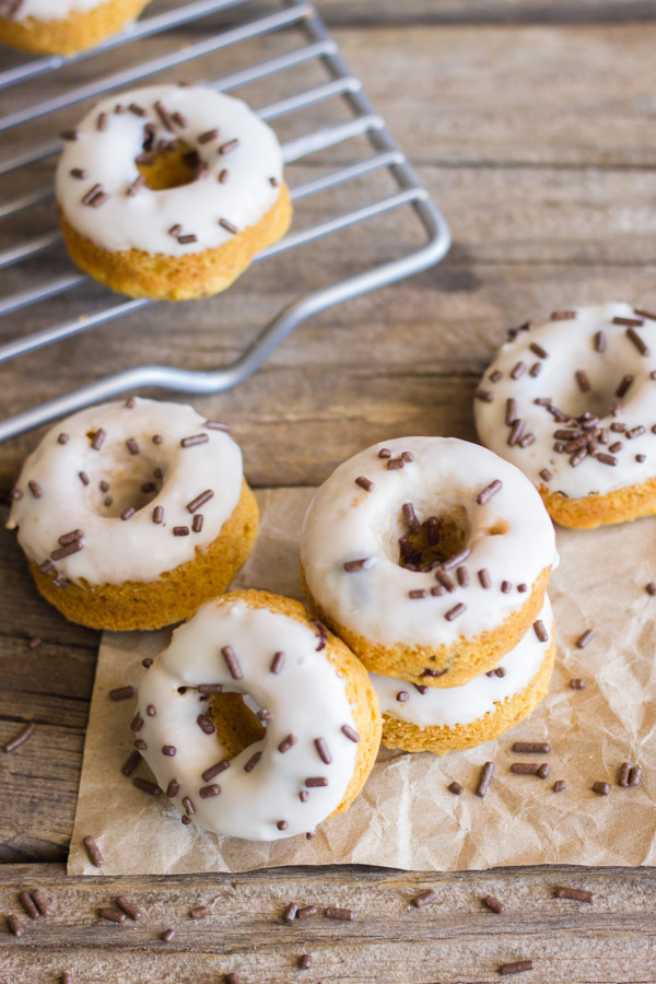 Mini Baked Pumpkin Chocolate Chip Donuts stacked on paper with sprinkles around them, with more Mini Baked Pumpkin Chocolate Chip Donuts on a cooling rack.