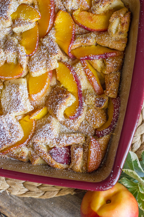 Peaches and Cream French Toast Bake in a baking dish with a whole peach sitting next to it.  