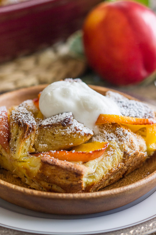 Peaches and Cream French Toast Bake topped with homemade whipped cream on a plate, and a whole peach in the background.  