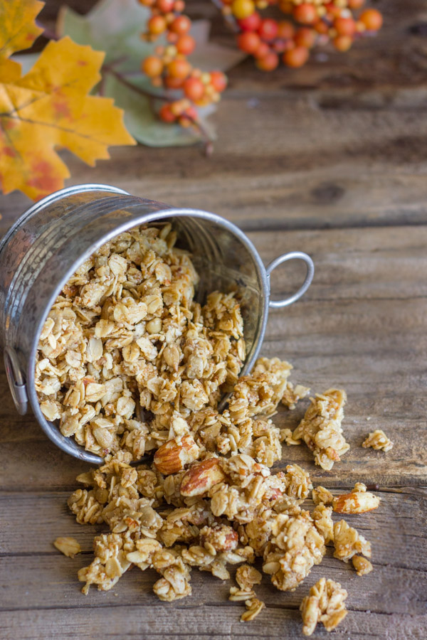 Pumpkin Pie Spice Coconut Oil Granola spilling out of a mini galvanized bucket, with fall decorations in the background. 