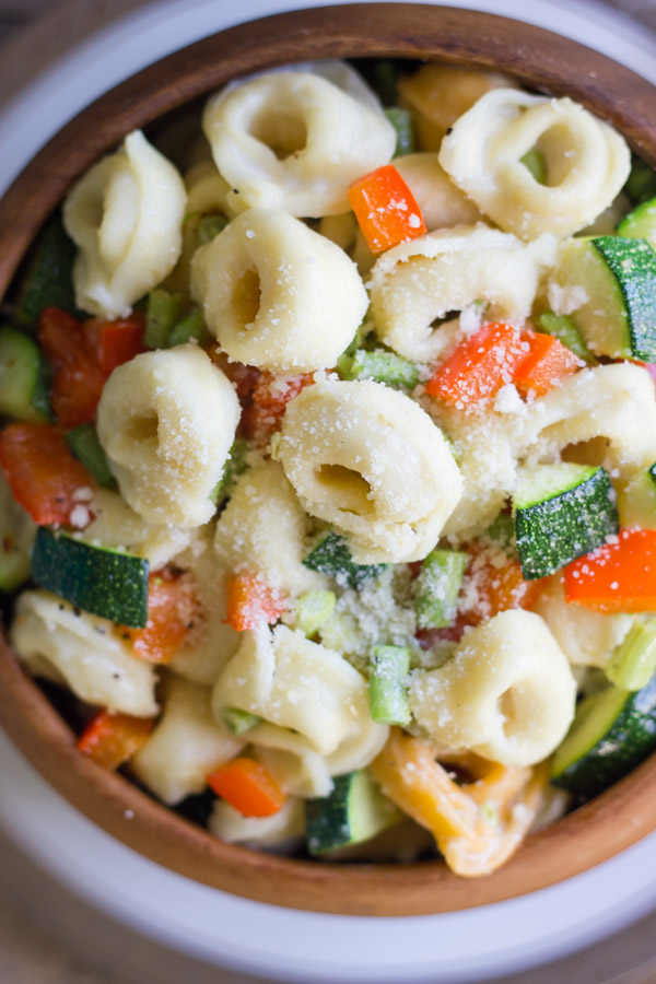 Vegetable Tortellini With Creamy Garlic Sauce in a wood bowl sitting on a plate.