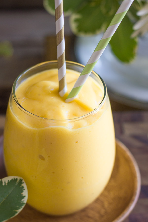 Tropical Sunshine Smoothie in a glass with two straws sitting on a little wood saucer.