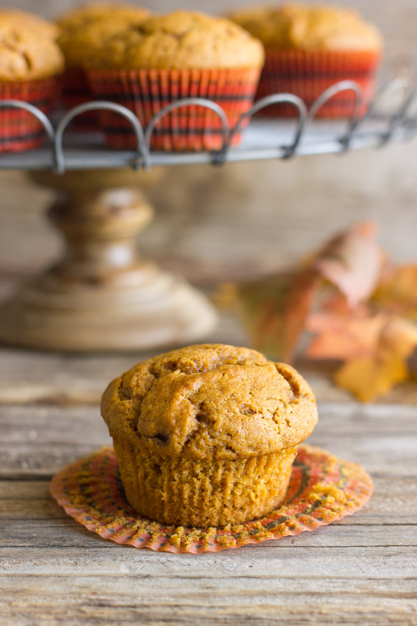 Best Ever Pumpkin Muffin with its wrapper pulled down and more muffins on a metal cake stand in the background.  