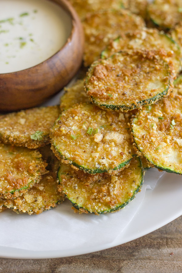 Pita Chip Fried Zucchini on a serving plate with a small bowl of ranch dressing.  