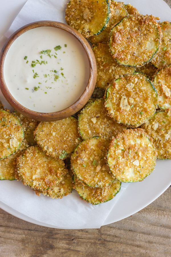 Pita Chip Fried Zucchini on a serving plate with a small bowl of ranch dressing.  