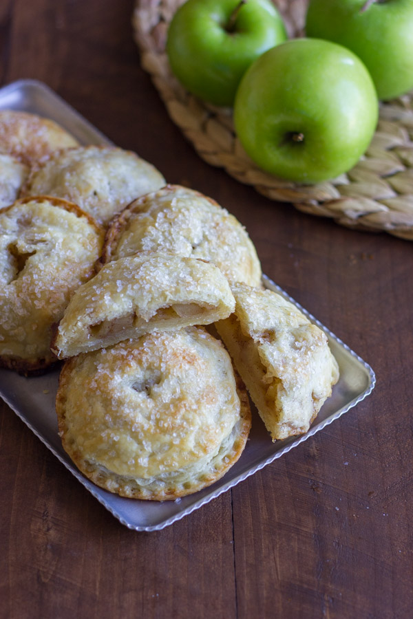 Apple Hand Pies on a serving platter, with one of the Apple Hand Pies cut in half, and some whole apples next to the platter.  