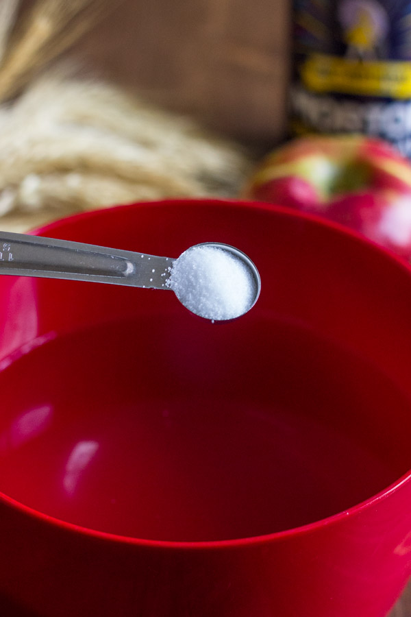 A measuring spoon of salt being poured into a bowl of water.  