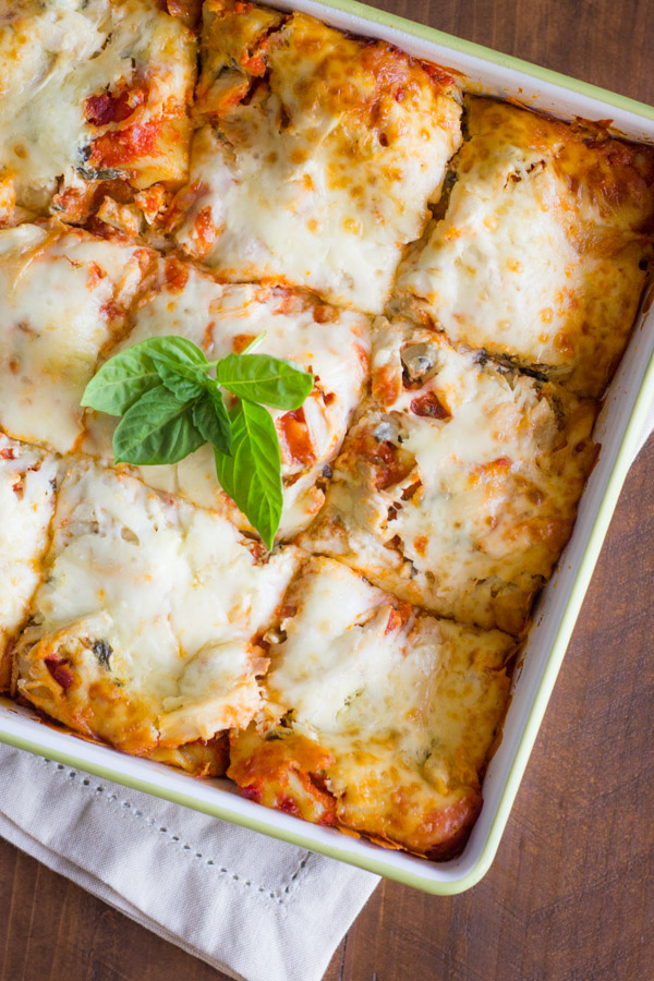 Spinach and Artichoke Chicken Lasagna in a baking dish, sliced into nine square pieces and topped with fresh basil leaves.  