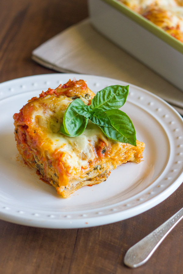 Spinach and Artichoke Chicken Lasagna square piece on a plate, topped with fresh basil leaves. 