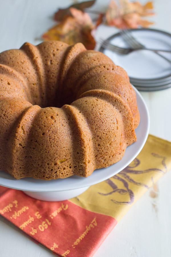 Pumpkin Spice Bundt Cake on a cake stand, with a stack of plates and forks in the background.  