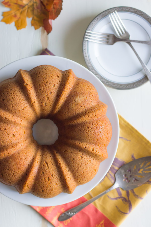 Pumpkin Spice Bundt Cake on a cake stand, with a serving utensil and a plate with forks next to the stand.  