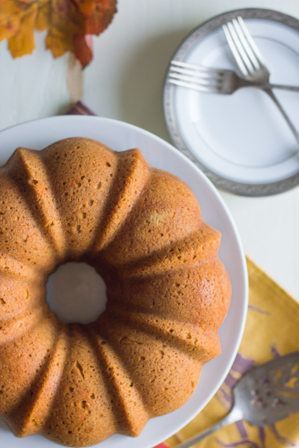 Pumpkin Spice Bundt Cake on a cake stand, with a serving utensil and a plate with forks next to the stand.  