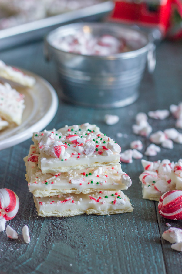 Butter Cracker Peppermint Bark squares stacked in a pile of three, with peppermint candy pieces around them.  