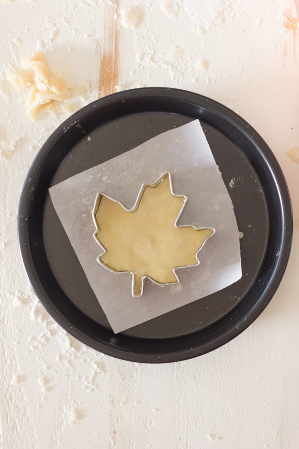 Pie Crust Tutorial Step 7 - leaf shaped cookie cutter with pie dough on parchment paper in a baking pan. 