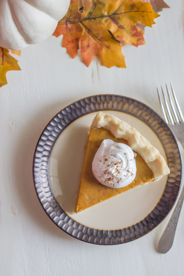 Classic Pumpkin Pie piece on a plate topped with whipped cream. 