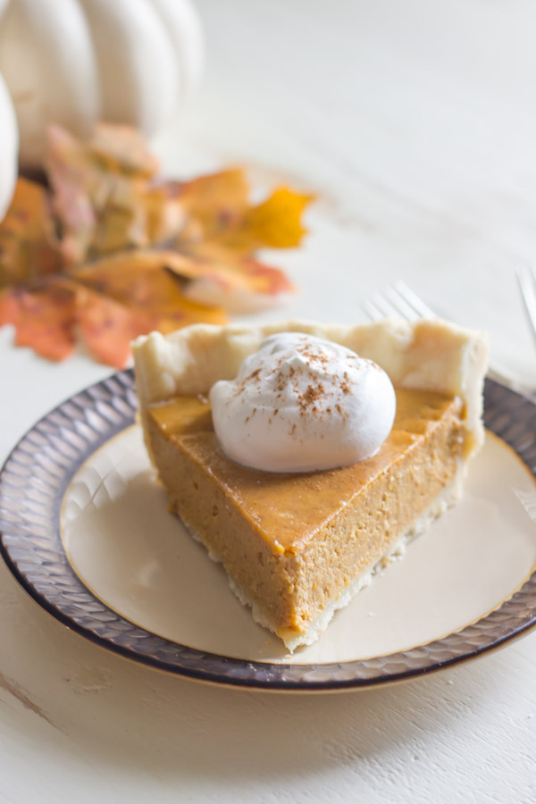 Classic Pumpkin Pie piece on a plate topped with whipped cream. 