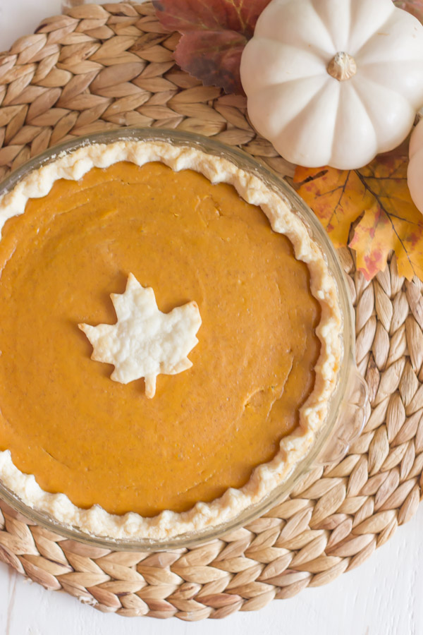 A whole Classic Pumpkin Pie with a leaf decoration, on a placemat with a pumpkin and fall leaves. 