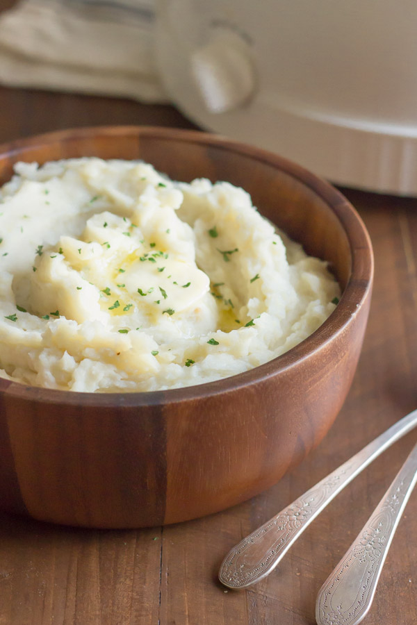 Easy Creamy Crockpot Roasted Garlic Mashed Potatoes in a bowl with butter and dried parsley on top.  
