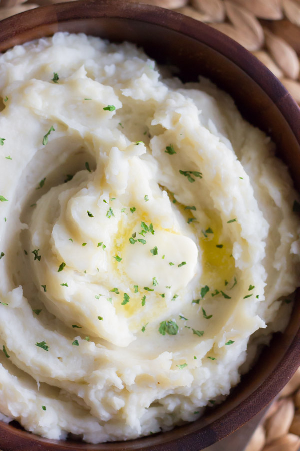 Top down view of Easy Crockpot Mashed potatoes in a wooden serving bowl with a pat of butter on top. 