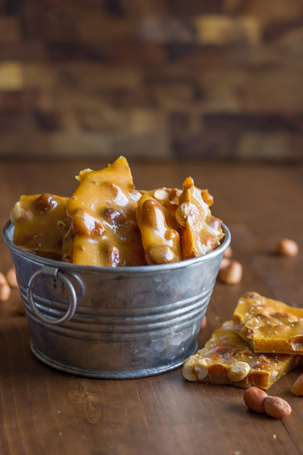 Peanut Brittle in a small galvanized bucket, with some pieces and peanuts next to it. 