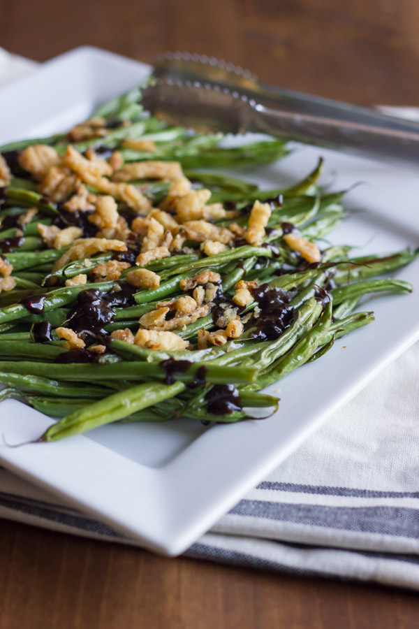 Roasted Green Beans with Creamy Cranberry Balsamic topped with french friend onions on a serving plate with tongs.  