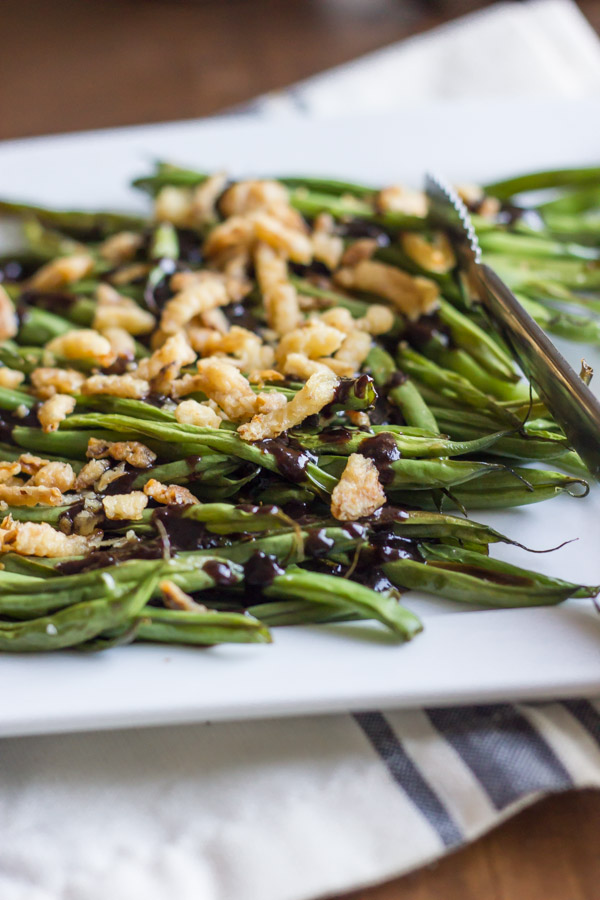 Roasted Green Beans with Creamy Cranberry Balsamic topped with french friend onions on a serving plate with tongs. 