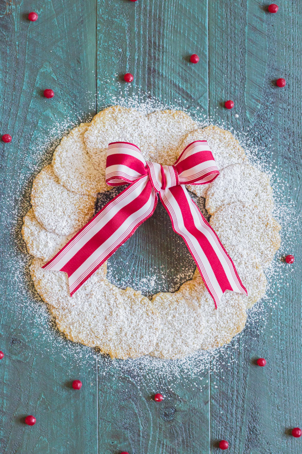 Christmas Oatmeal Cookies dusted with powdered sugar and arranged in a circle to look like a wreath with a red and white striped bow.  