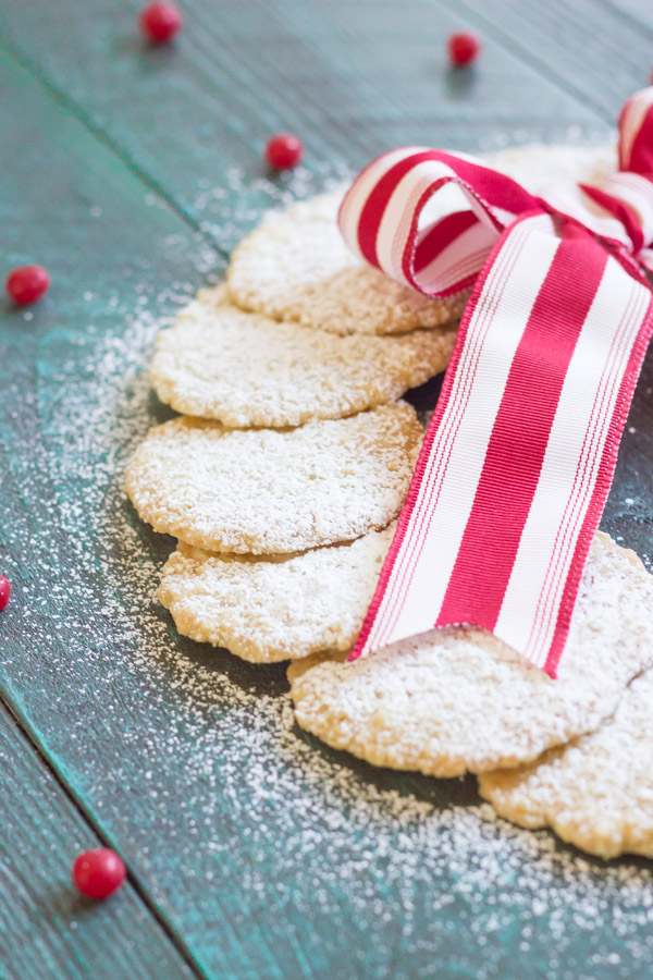 Christmas Oatmeal Cookies dusted with powdered sugar and arranged in a circle to look like a wreath with a red and white striped bow.  