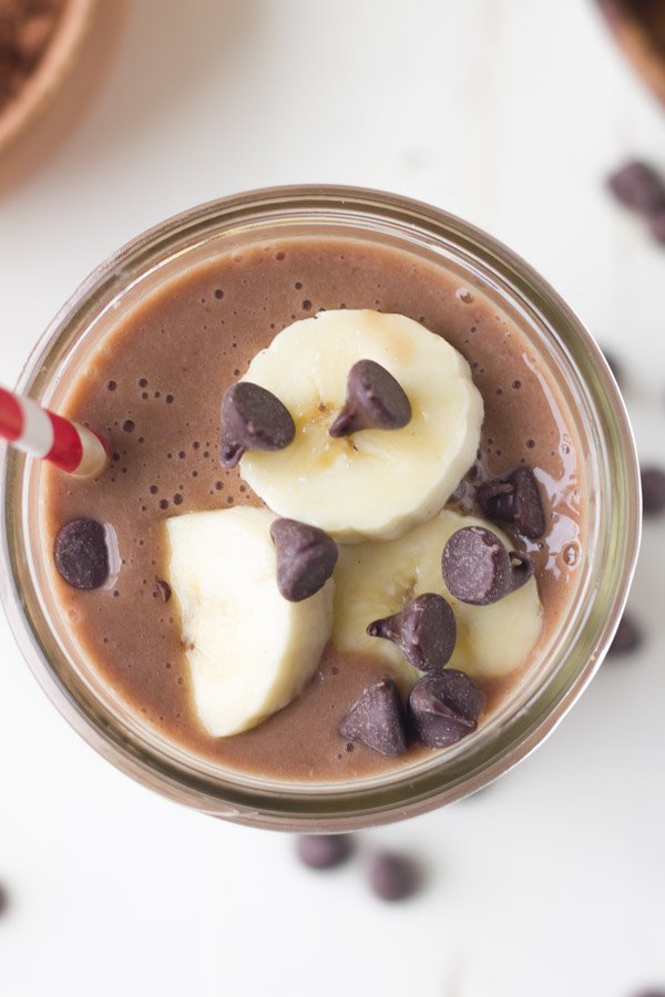 Chocolate Banana Smoothie topped with banana slices and chocolate chips, in a glass jar with a straw.