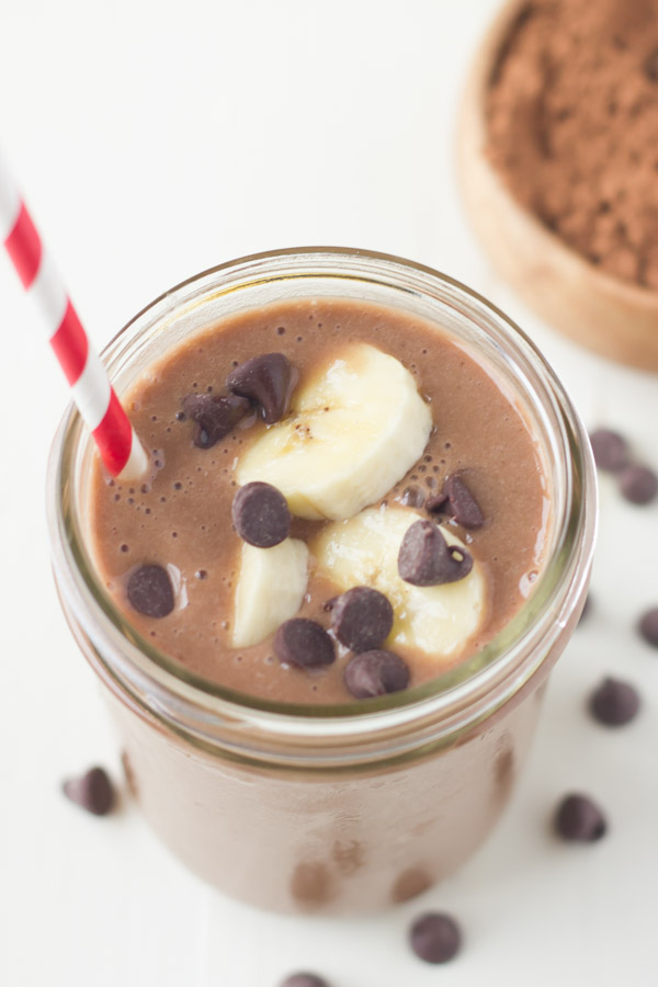 Chocolate Banana Smoothie topped with banana slices and chocolate chips, in a glass jar with a straw.